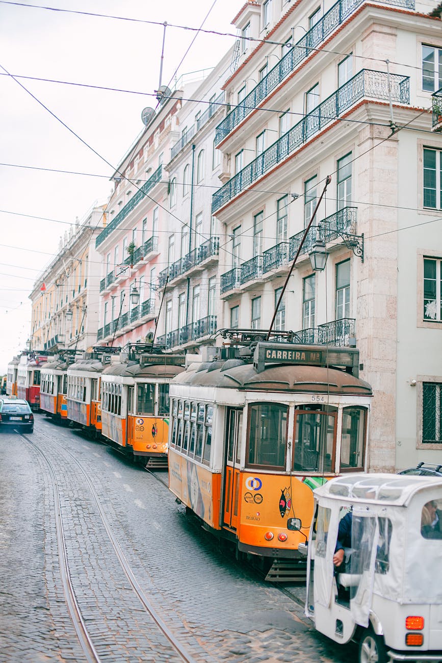 A picturesque view of traditional yellow trams winding through a cobblestone street in Lisbon, flanked by charming buildings with balconies.