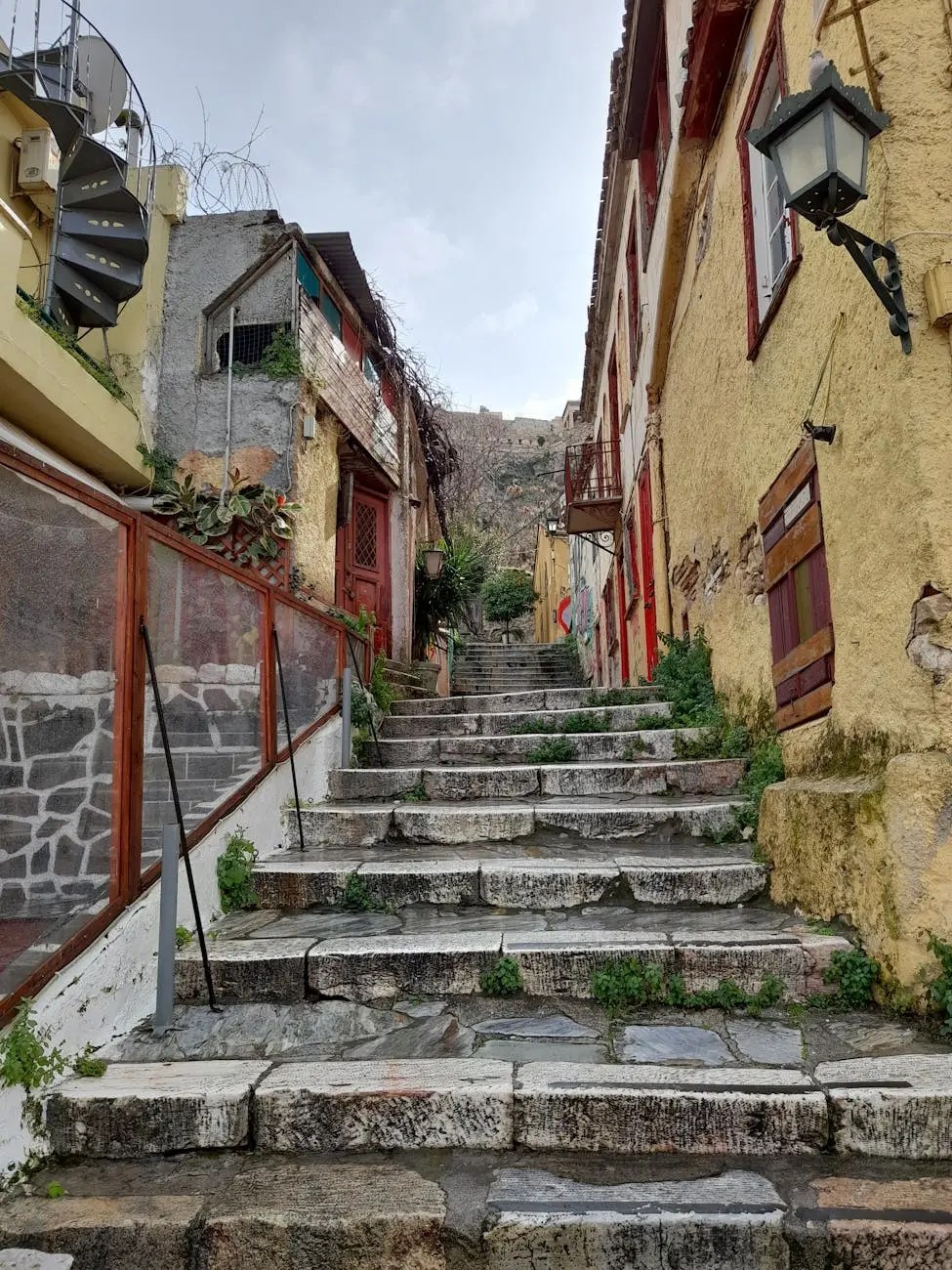 A picturesque stone stairway leading through a narrow, charming street in Athens, lined with colorful buildings and lush greenery.