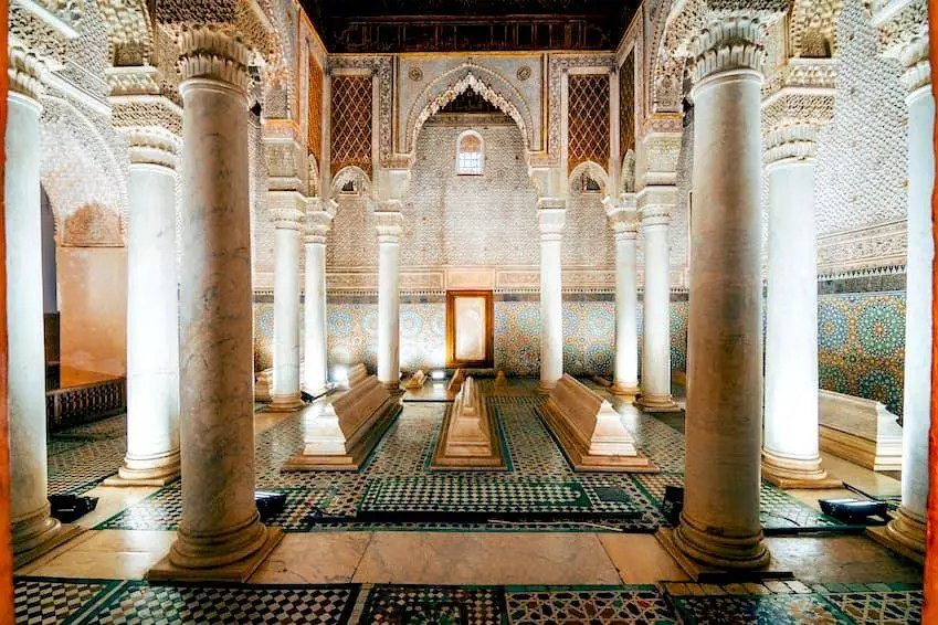 Interior view of a historical Moroccan palace with tall columns, intricate tile work, and ornate arches, showcasing a serene atmosphere and decorative elements.
