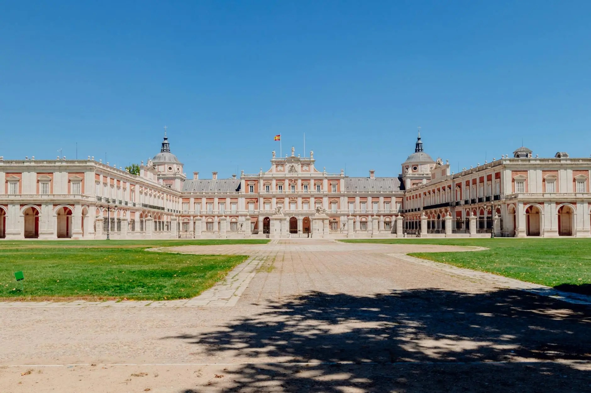 The wide view of a grand historical palace with beautiful architecture, surrounded by a lush green lawn under a clear blue sky.
