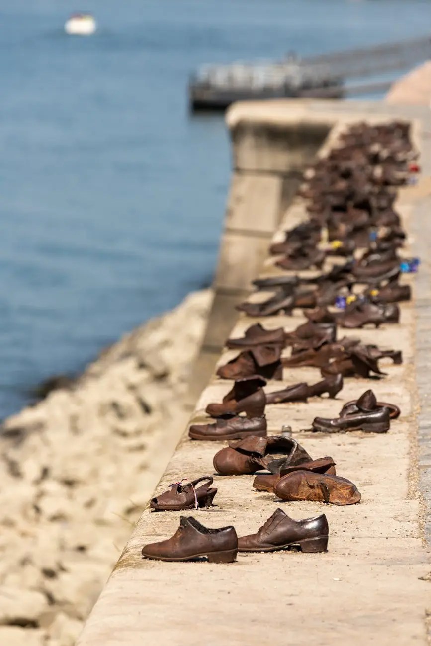 A memorial featuring a series of old brown shoes placed along a stone riverbank, with the Danube River in the background.