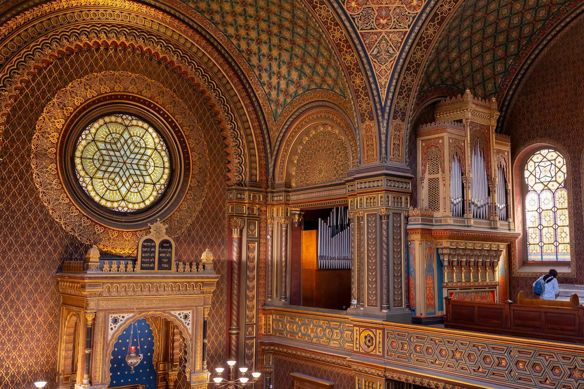Interior view of a beautifully ornate synagogue featuring intricate patterns, colorful stained glass windows, and a large organ.