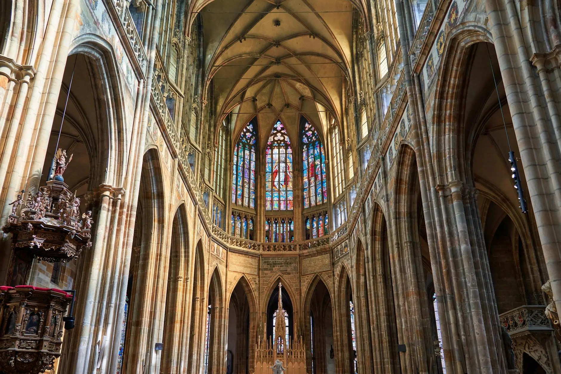 Interior view of St. Vitus Cathedral featuring gothic architectural elements and colorful stained glass windows.