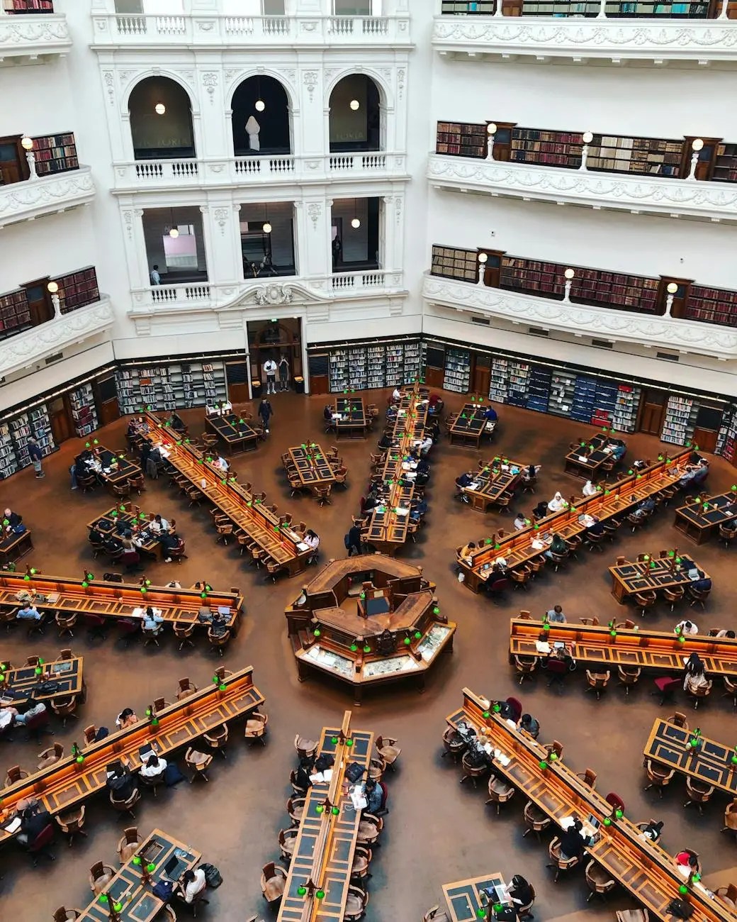 Interior view of a grand library featuring multiple reading tables and bookshelves, with people studying throughout the space.