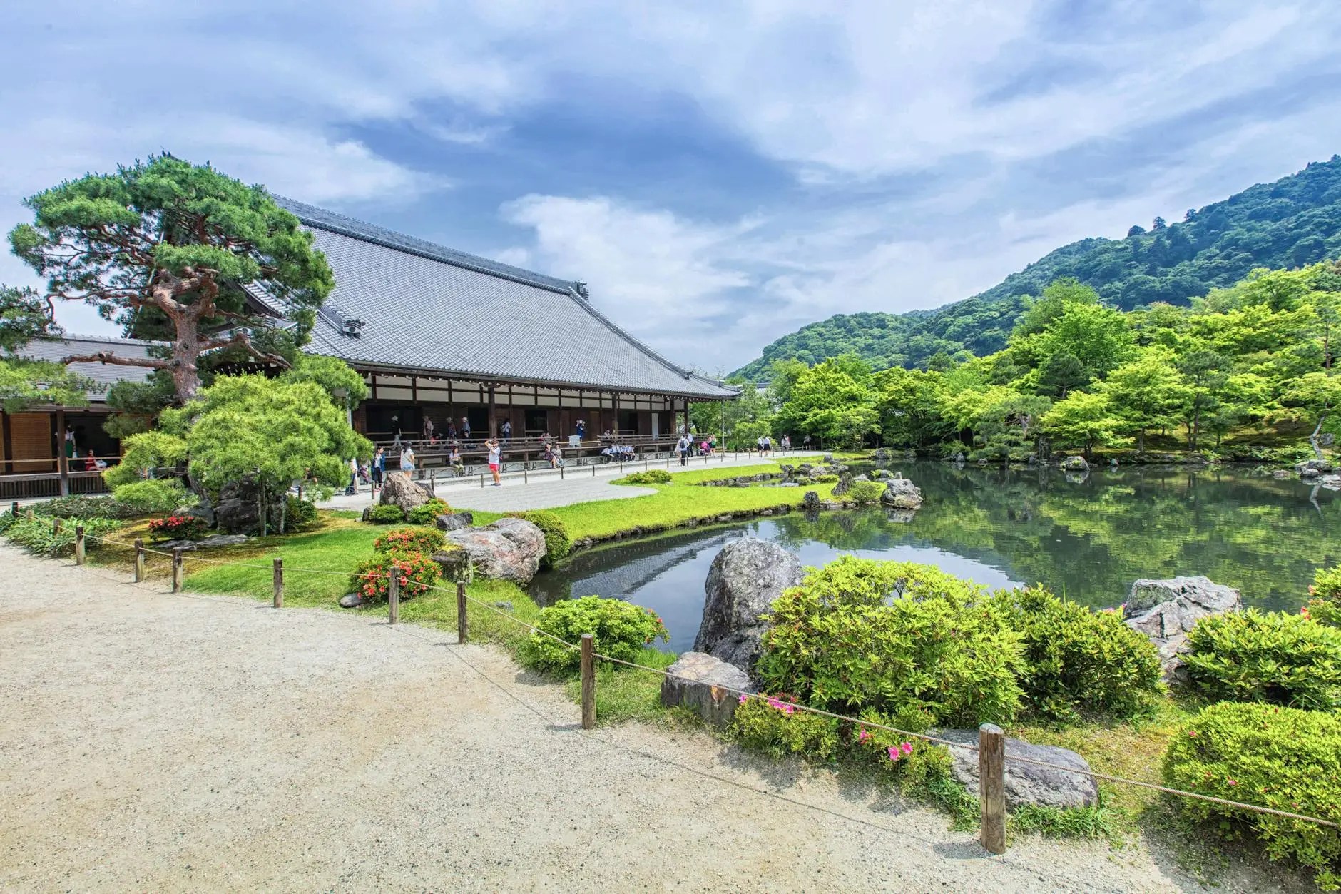 Scenic view of a traditional Japanese temple surrounded by lush greenery and a tranquil pond.
