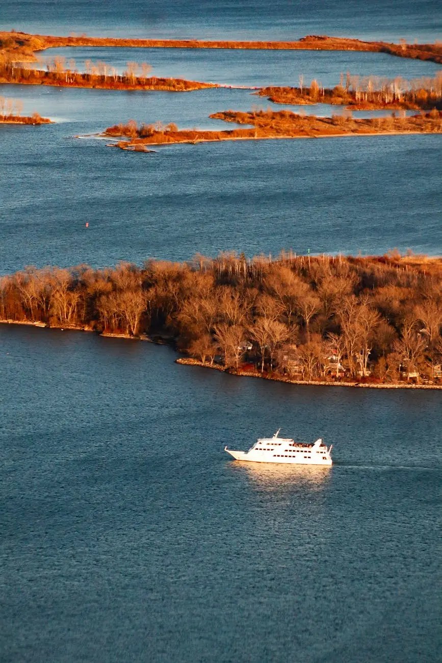 A scenic view of the Toronto Islands with a boat sailing in the foreground, surrounded by calm waters and autumn foliage.