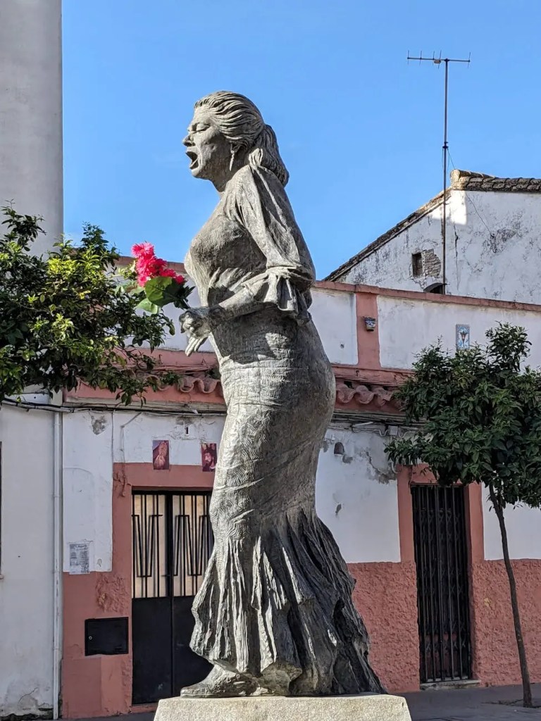 Statue of a flamenco dancer holding flowers, set against a backdrop of traditional Spanish architecture.