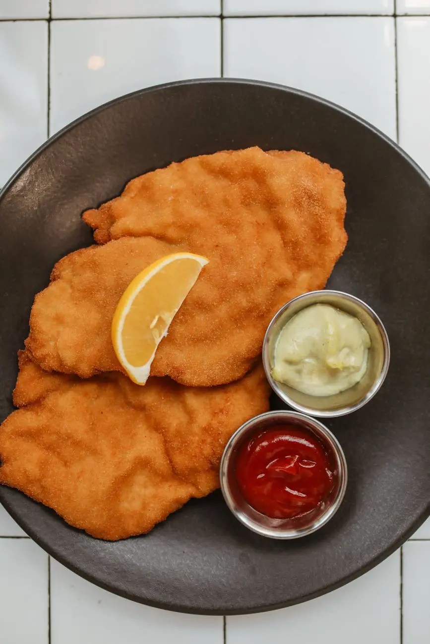 A plate of Wiener Schnitzel served with a slice of lemon and two small bowls of condiments: ketchup and mustard.