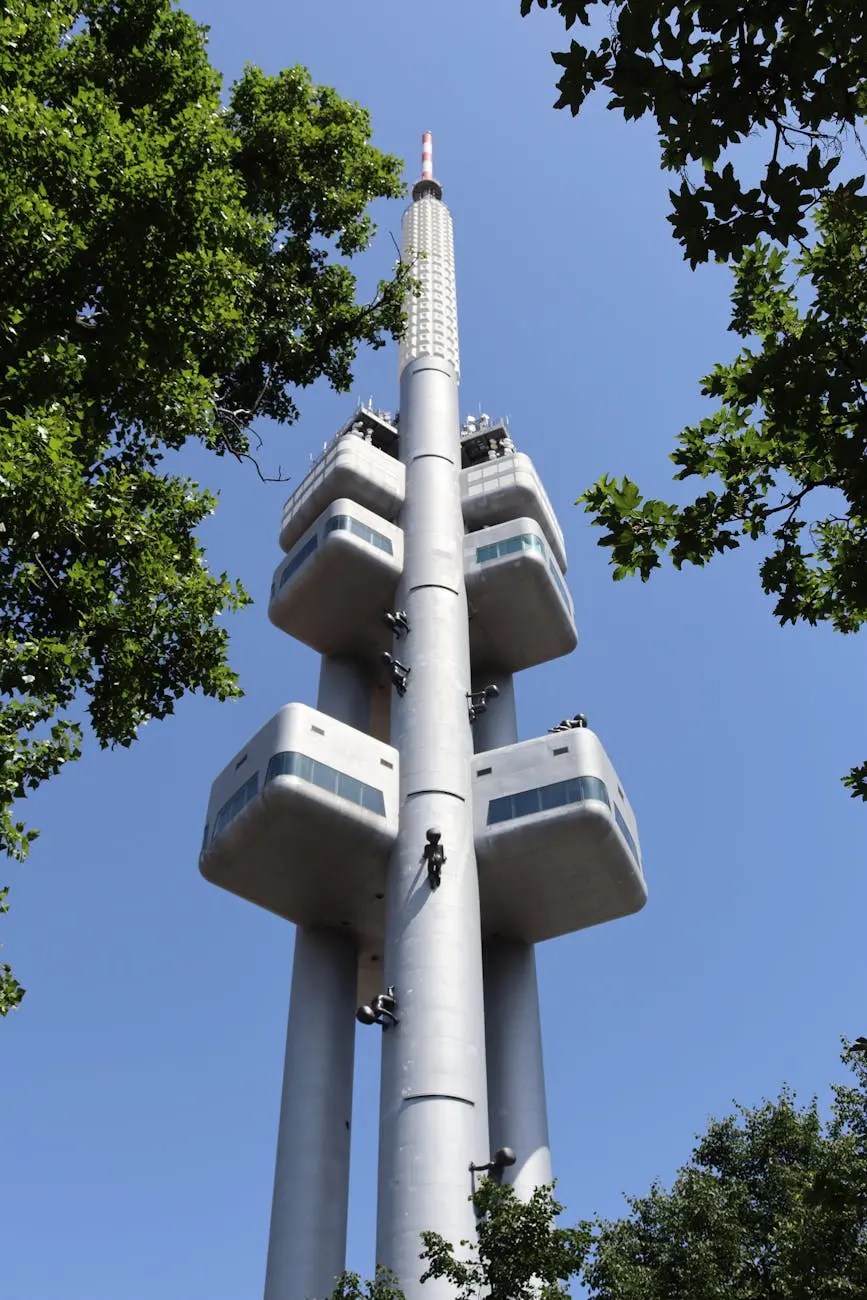 View of the Zizkov TV Tower in Prague, featuring its unique architectural design with viewing pods and trees in the foreground.