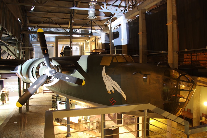 A historic aircraft displayed in a museum, featuring a prominent propeller and an eagle emblem, set within a modern architectural space.