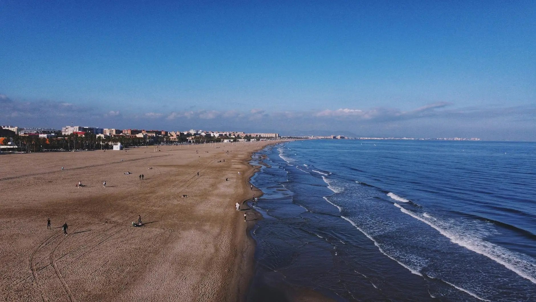 A scenic view of Valencia's Malvarrosa Beach, featuring golden sand, gentle waves lapping at the shore, and a clear blue sky above.
