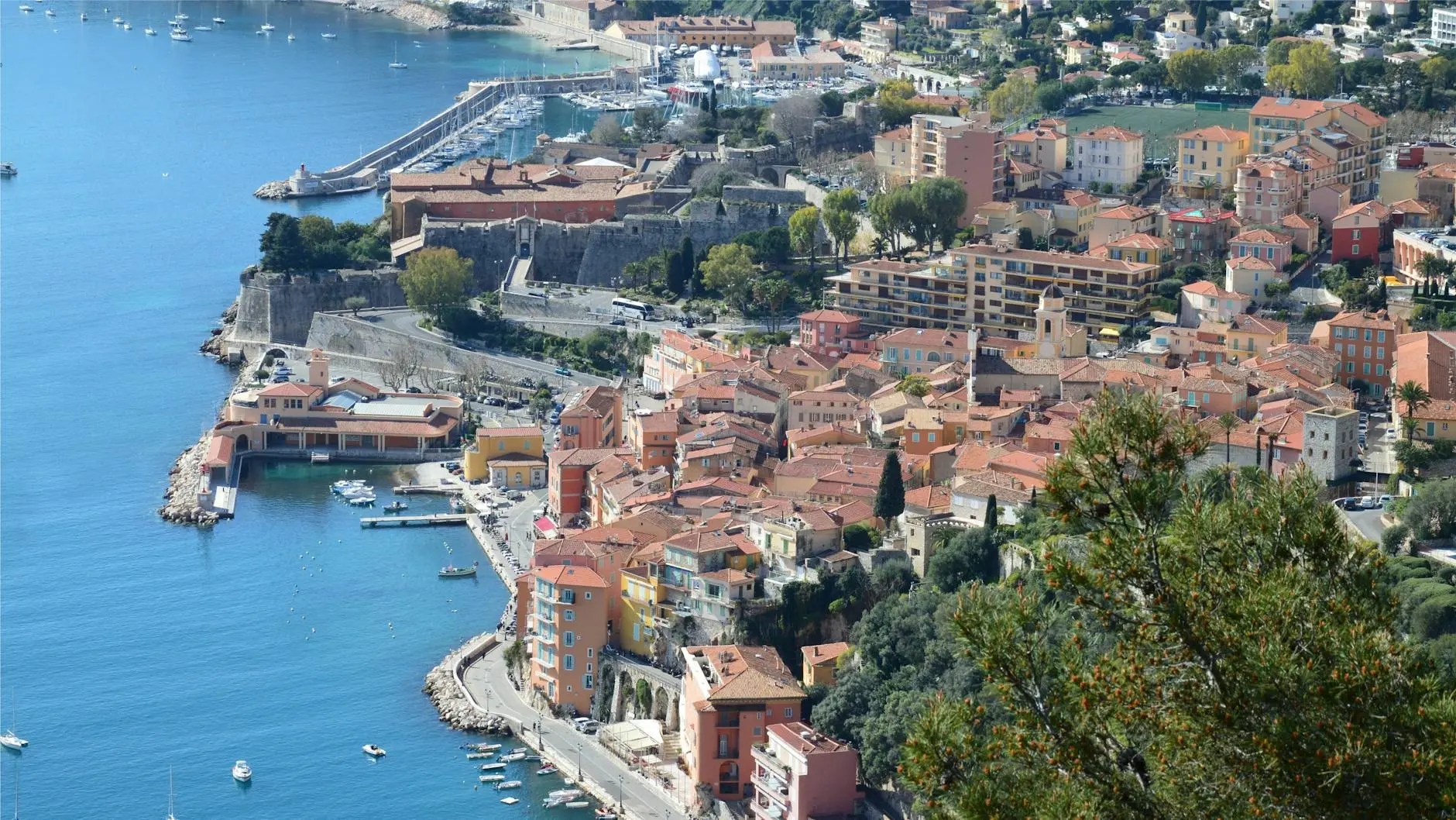 Aerial view of a picturesque coastal town on the French Riviera, showcasing colorful buildings, a marina with boats, and the serene blue waters of the Mediterranean Sea.