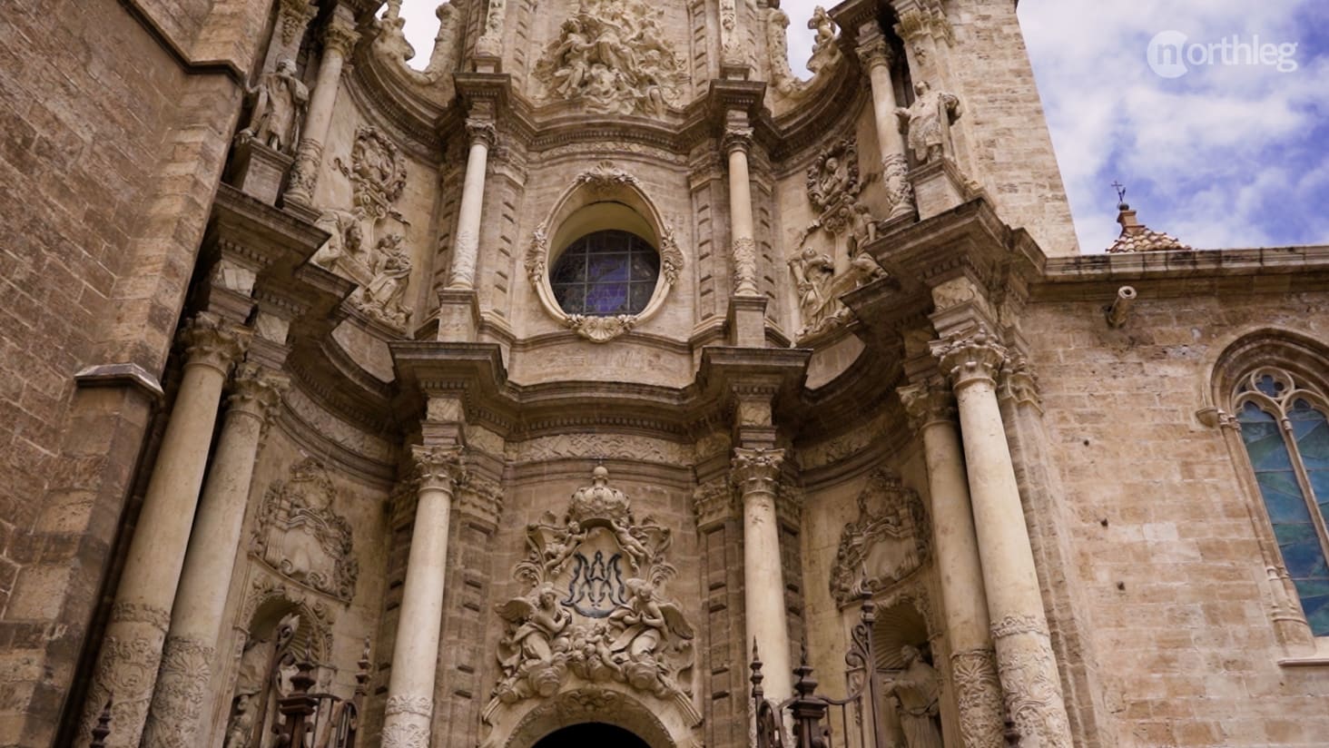 Close-up view of the ornate facade of a historic church in Valencia, featuring intricate sculptures, columns, and a stained glass window.