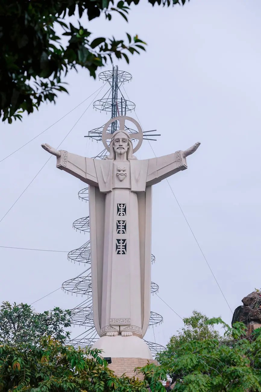 A large statue of Christ the Redeemer with outstretched arms, standing atop a hill surrounded by trees and a cloudy sky.