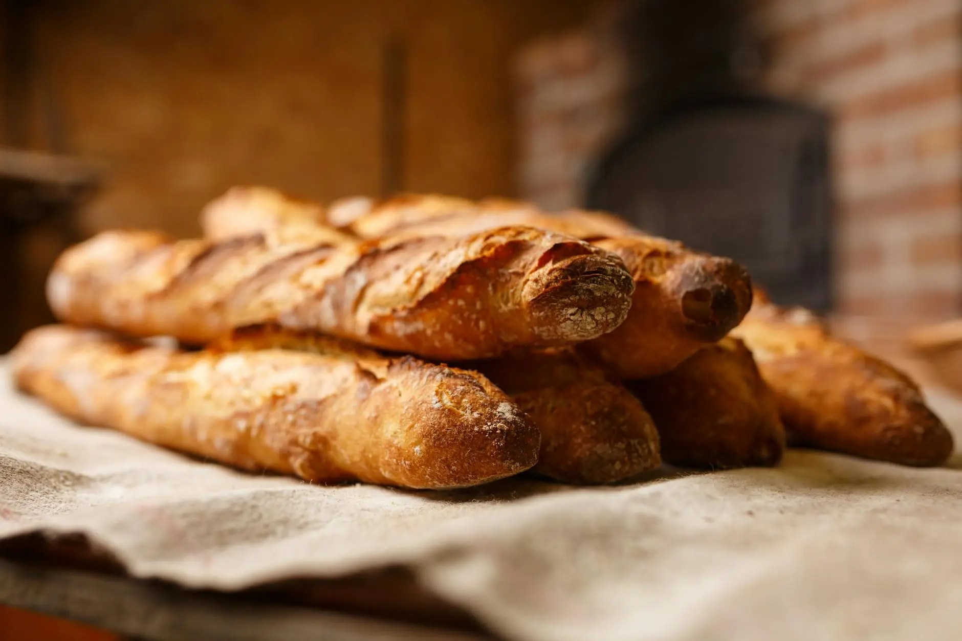 Freshly baked baguettes stacked on a wooden surface, showcasing a golden-brown crust with a rustic background.