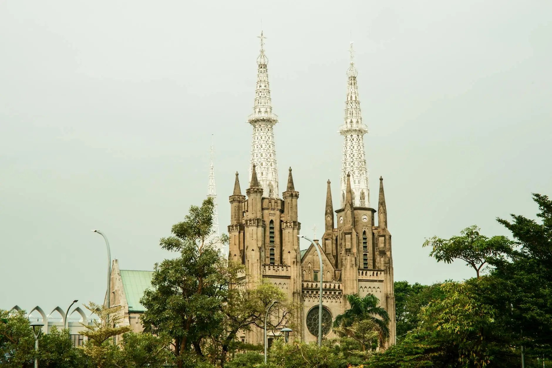 A historical church with tall, ornate spires and a mix of architectural styles, surrounded by trees and greenery in an urban setting.