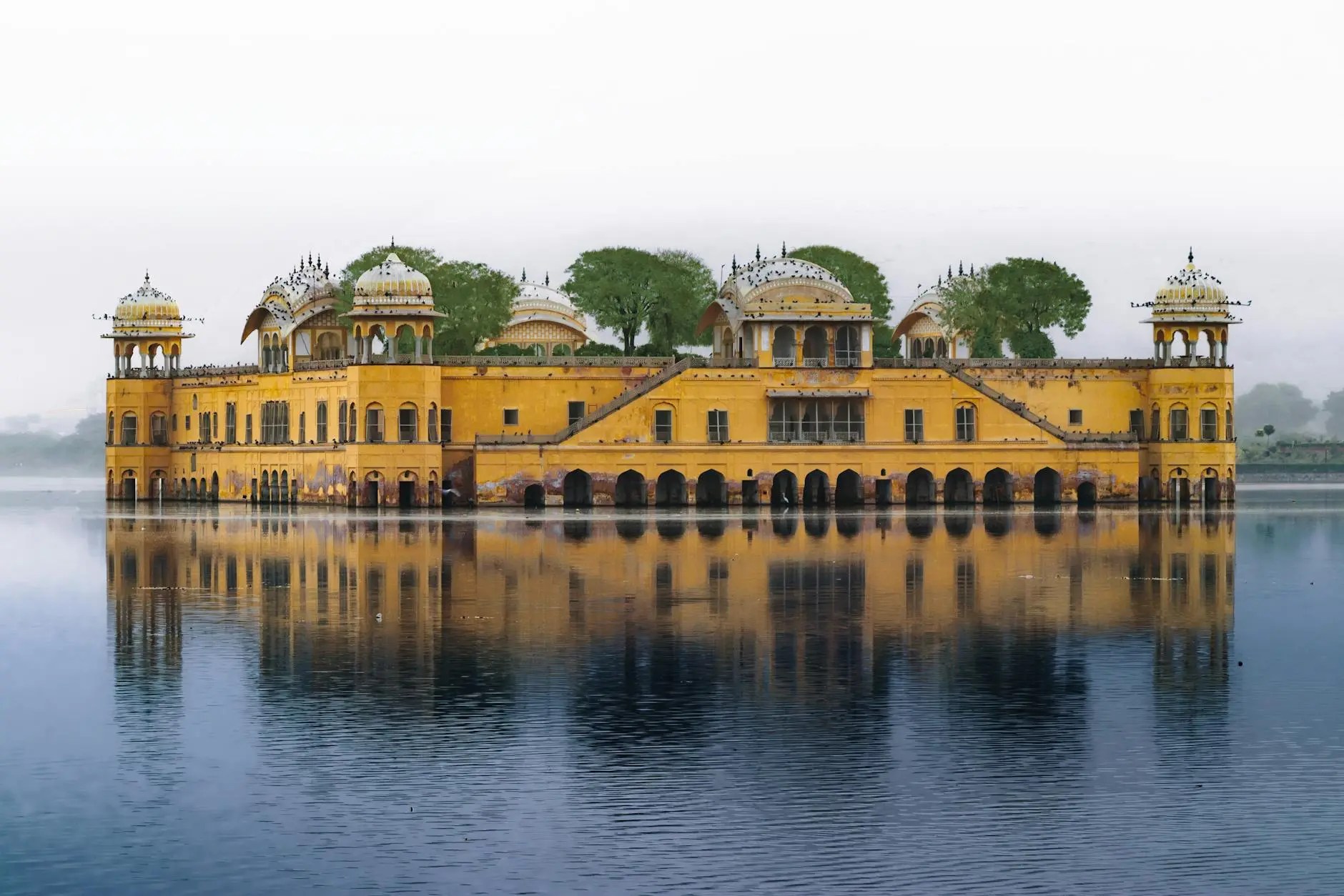 View of Jal Mahal, the Water Palace in Jaipur, reflecting in the calm waters of Man Sagar Lake, surrounded by lush greenery.