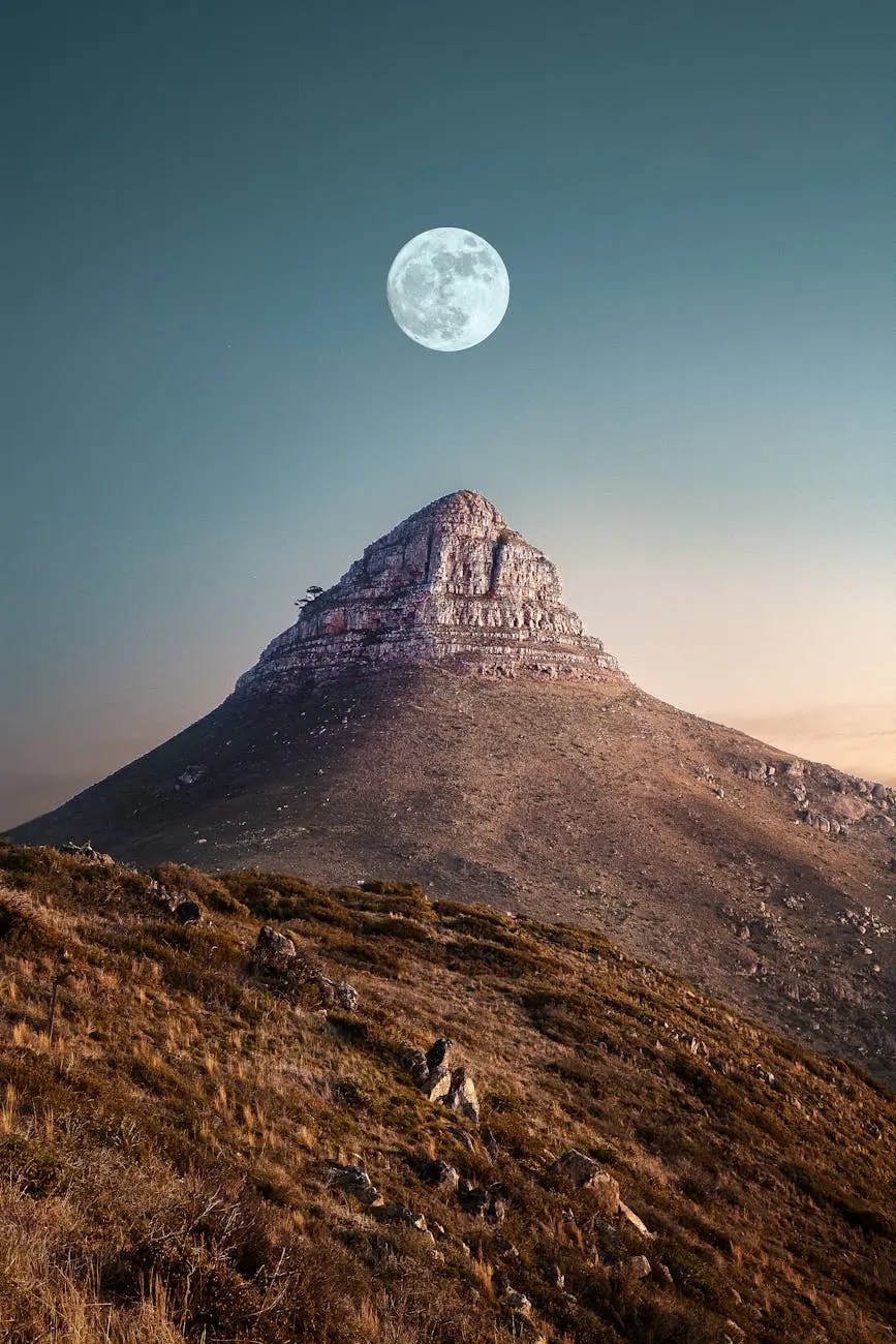 A scenic view of a mountain peak under a clear sky with a large full moon in the background, showcasing the natural beauty of the landscape.