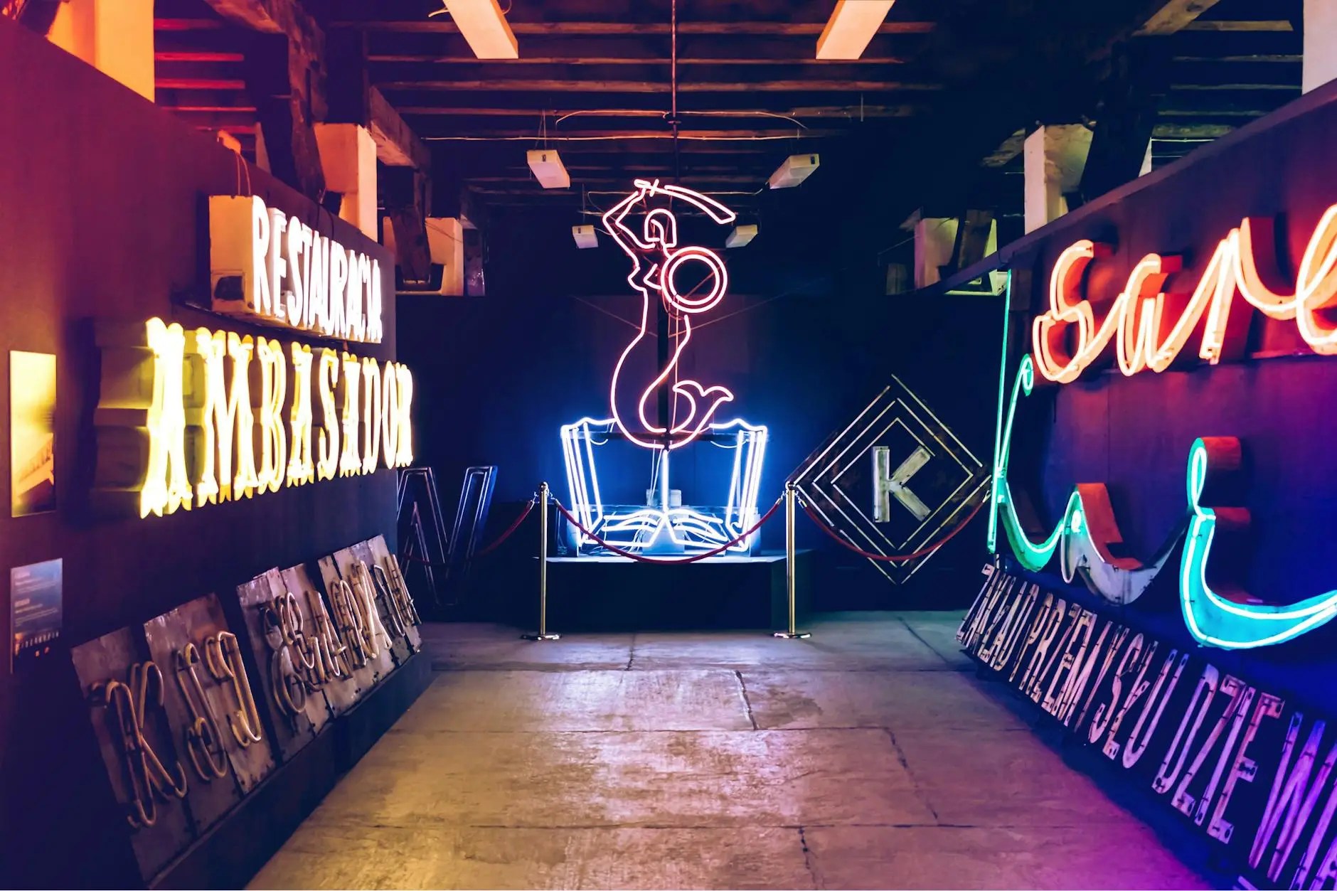 An exhibition featuring colorful neon signs and art installations, including a prominent neon figure, set in a dimly lit room.