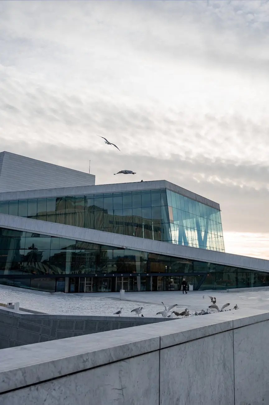 The Oslo Opera House, showcasing modern architecture with glass and white marble, under a cloudy sky, featuring seagulls flying above.