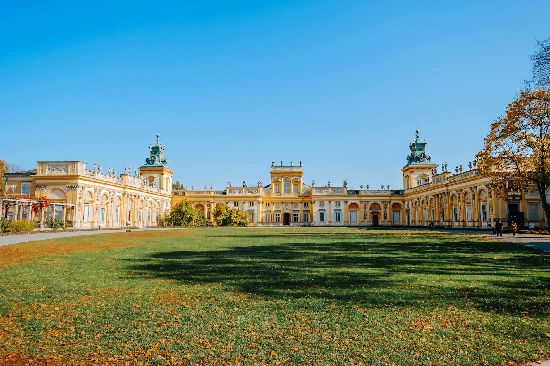 The exterior of Łazienki Palace surrounded by green grass and clear blue skies in Warsaw, Poland.