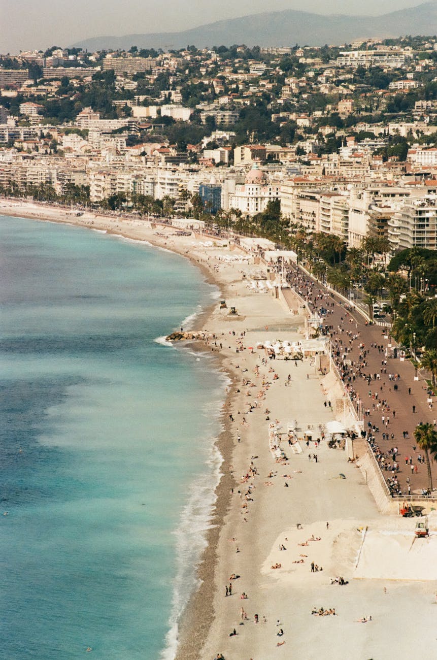 Aerial view of the beach and coastline of Nice, France, featuring sandy shores, the Mediterranean sea, and the urban area along the waterfront.