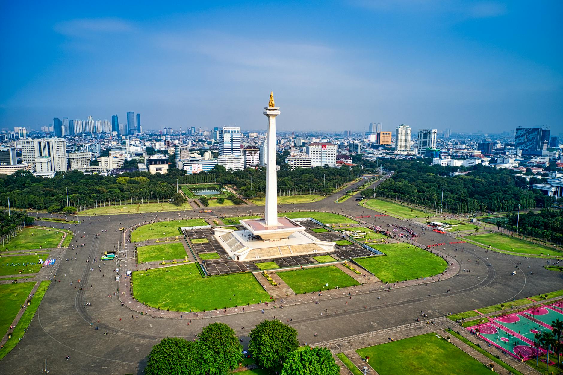 Aerial view of Jakarta's National Monument surrounded by green spaces and city skyline.
