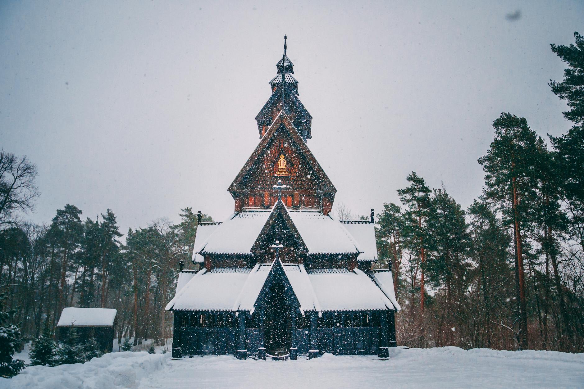 A traditional wooden church in Norway covered in snow, surrounded by snow-laden trees.