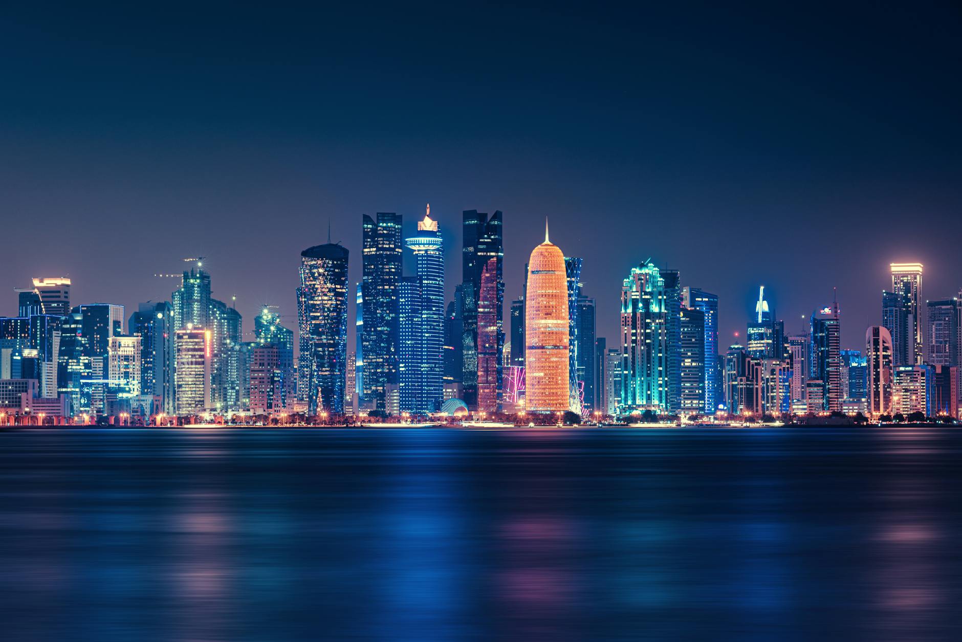A stunning view of the Doha skyline at night, showcasing skyscrapers illuminated with vibrant lights reflecting on the water.