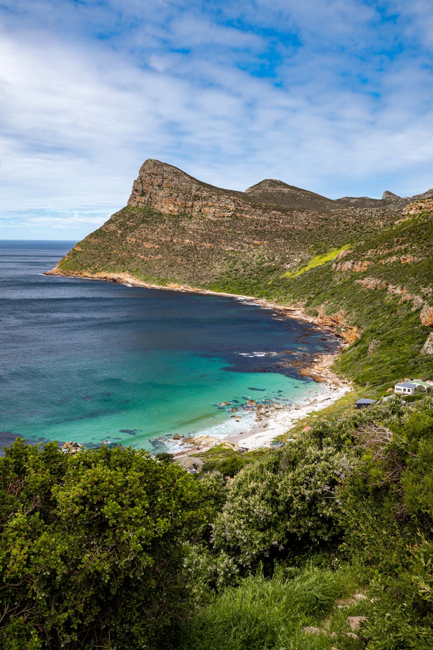 A scenic view of a beach cove surrounded by rocky hills, featuring turquoise waters and lush greenery in the foreground.
