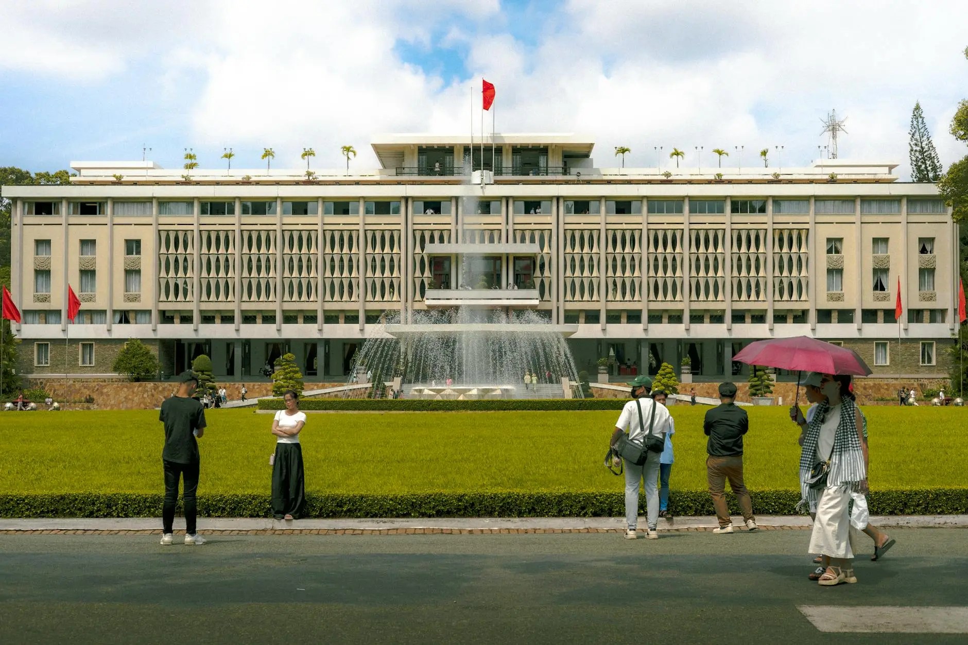The Reunification Palace in Ho Chi Minh City, featuring a fountain in front and visitors interacting in the foreground.