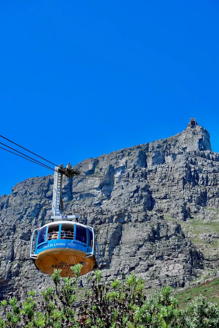 Aerial view of the Table Mountain Cableway in Cape Town, South Africa, with a blue sky and rocky mountain backdrop.