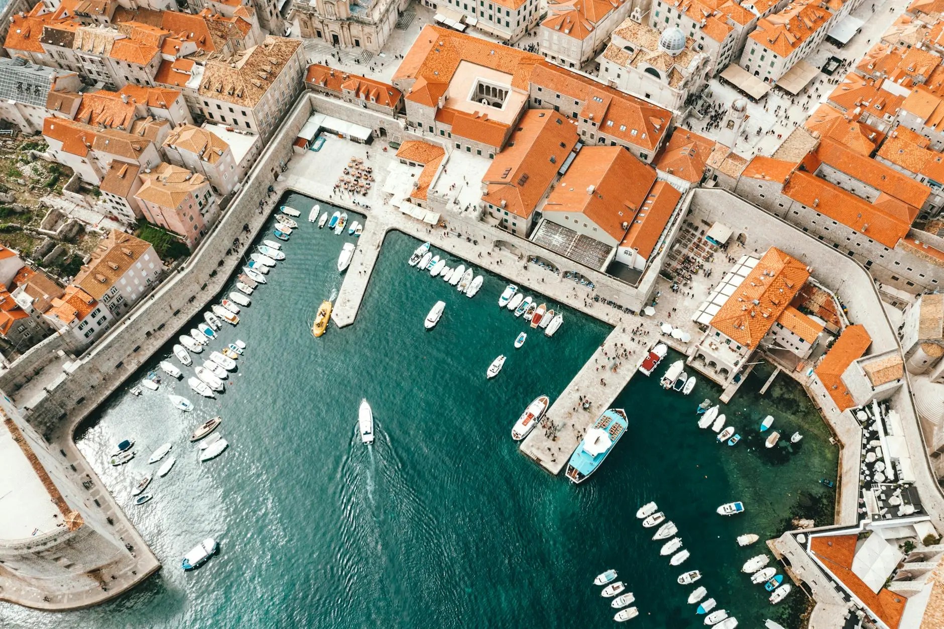 Aerial view of Dubrovnik's old town featuring terracotta rooftops, city walls, and a bustling harbor with various boats docked.