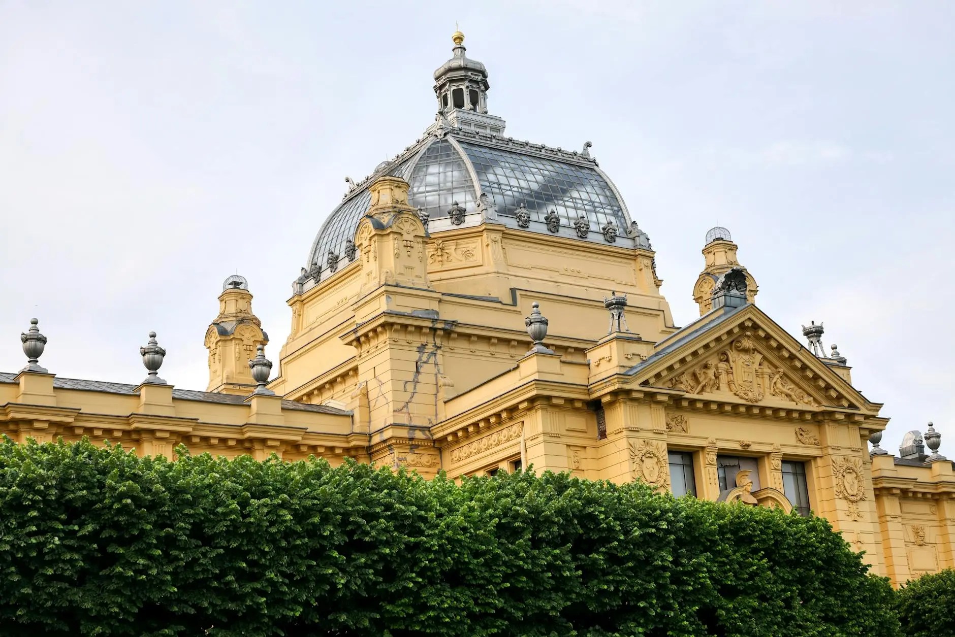 Close-up view of the ornate dome and architecture of a historic yellow building, partially obscured by green foliage.