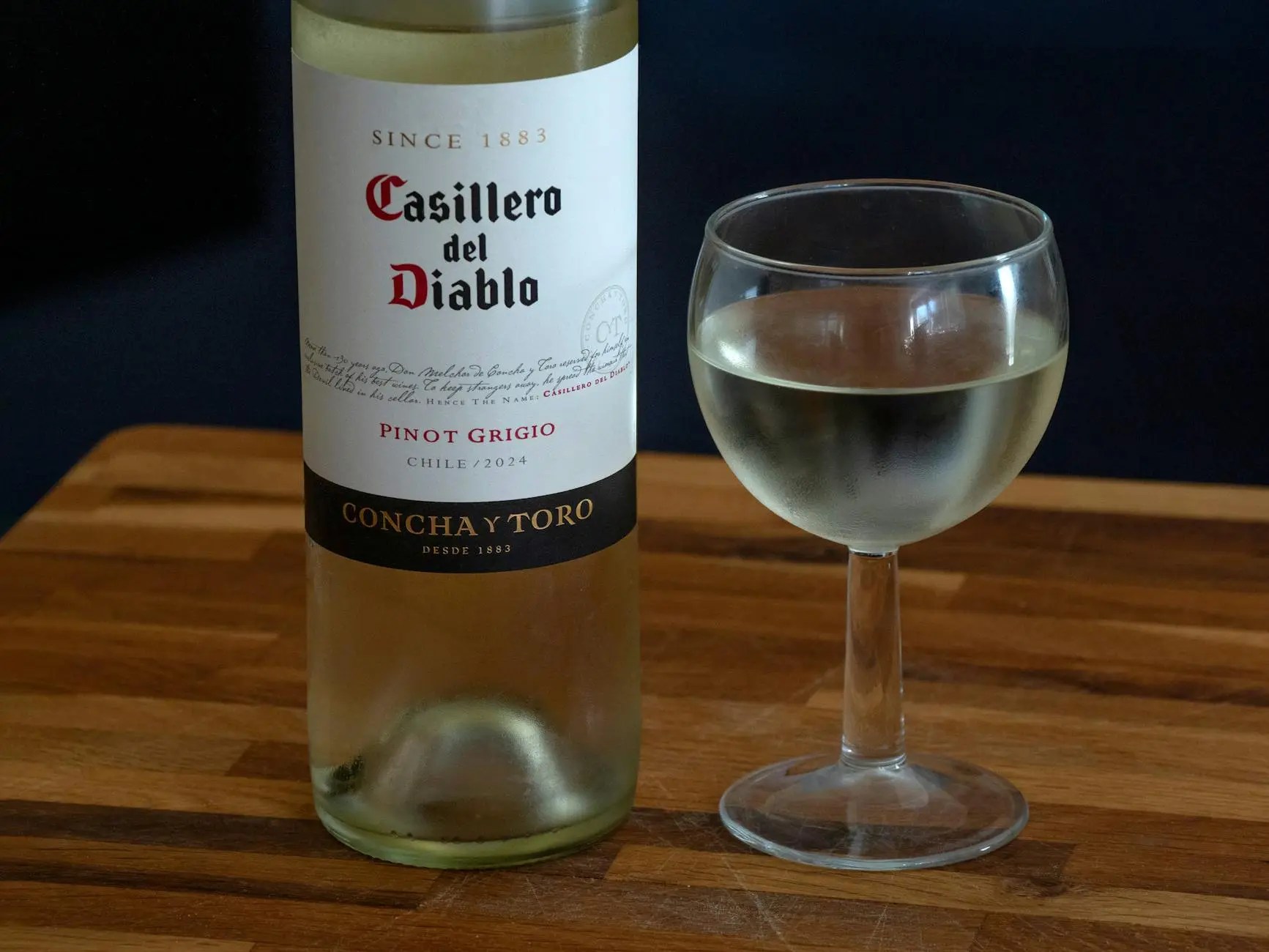 A bottle of Casillero del Diablo Pinot Grigio from Chile, 2024 vintage, displayed next to a glass filled with the white wine on a wooden surface.