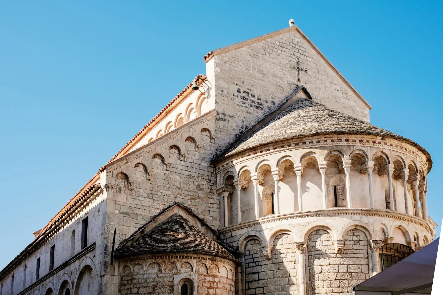 View of a historical church in Zadar, Croatia, showcasing its stone architecture and decorative arches against a bright blue sky.