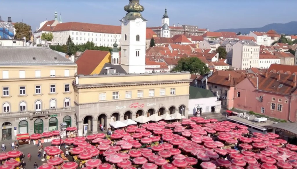 Aerial view of Zagreb's Dolac Market featuring vibrant red umbrellas amidst historic buildings and rooftops.