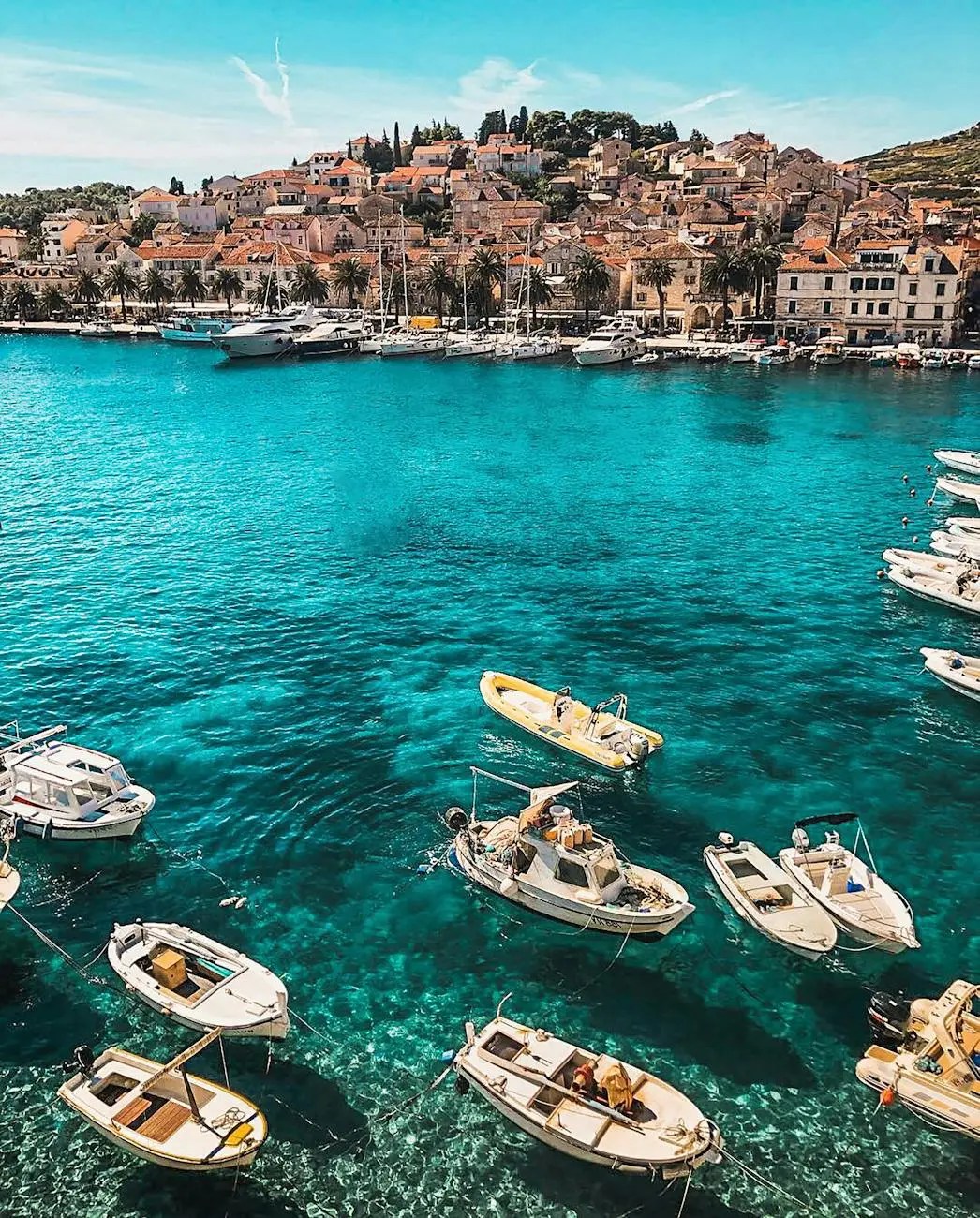 A picturesque view of a harbor in Croatia, featuring numerous small boats on crystal-clear turquoise water, surrounded by charming coastal buildings and lush greenery.
