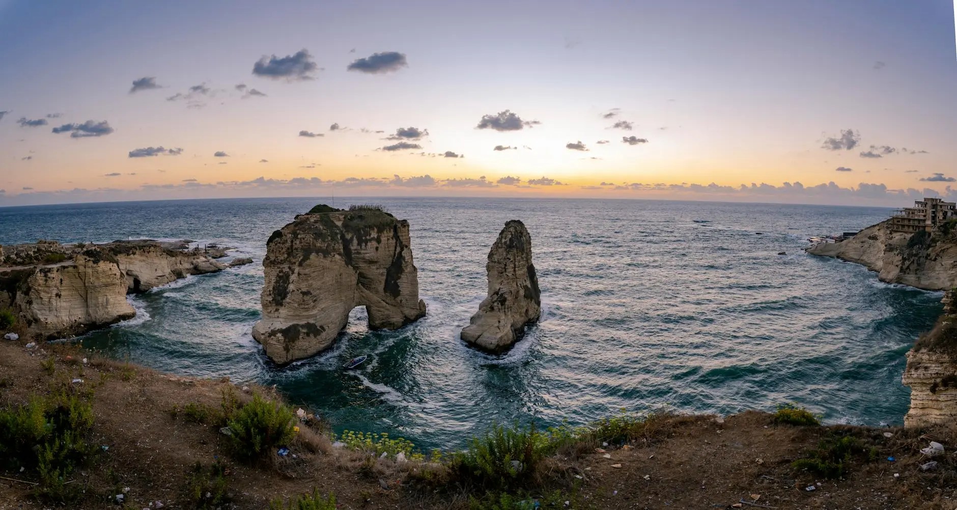 Panoramic view of the Pigeon Rocks in Raouché, Beirut, at sunset, with the tranquil Mediterranean Sea and a colorful sky.