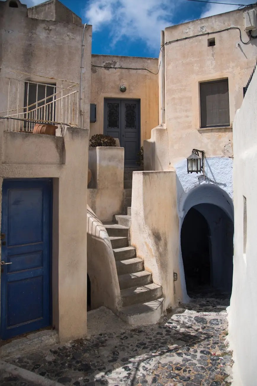 Narrow alleyway with traditional white buildings and a blue door in Santorini, Greece, featuring stone steps and a serene atmosphere.
