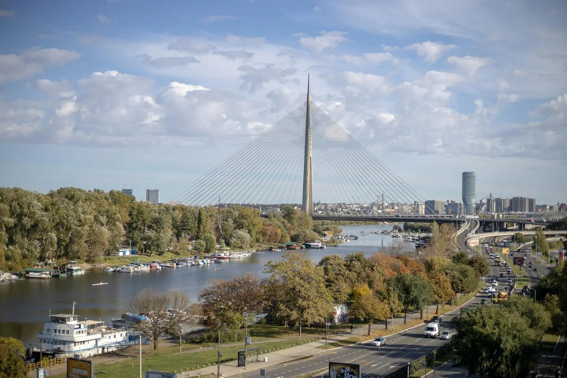View of the Sava River with a suspension bridge in Belgrade, Serbia, featuring lush greenery along the shoreline and a skyline in the background.