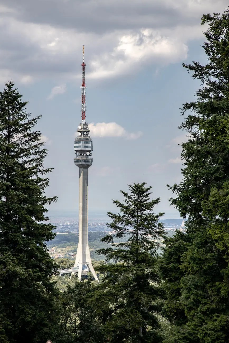 The Avala Tower surrounded by lush green trees, with a cloudy sky in the background, showcasing a modern architectural structure.