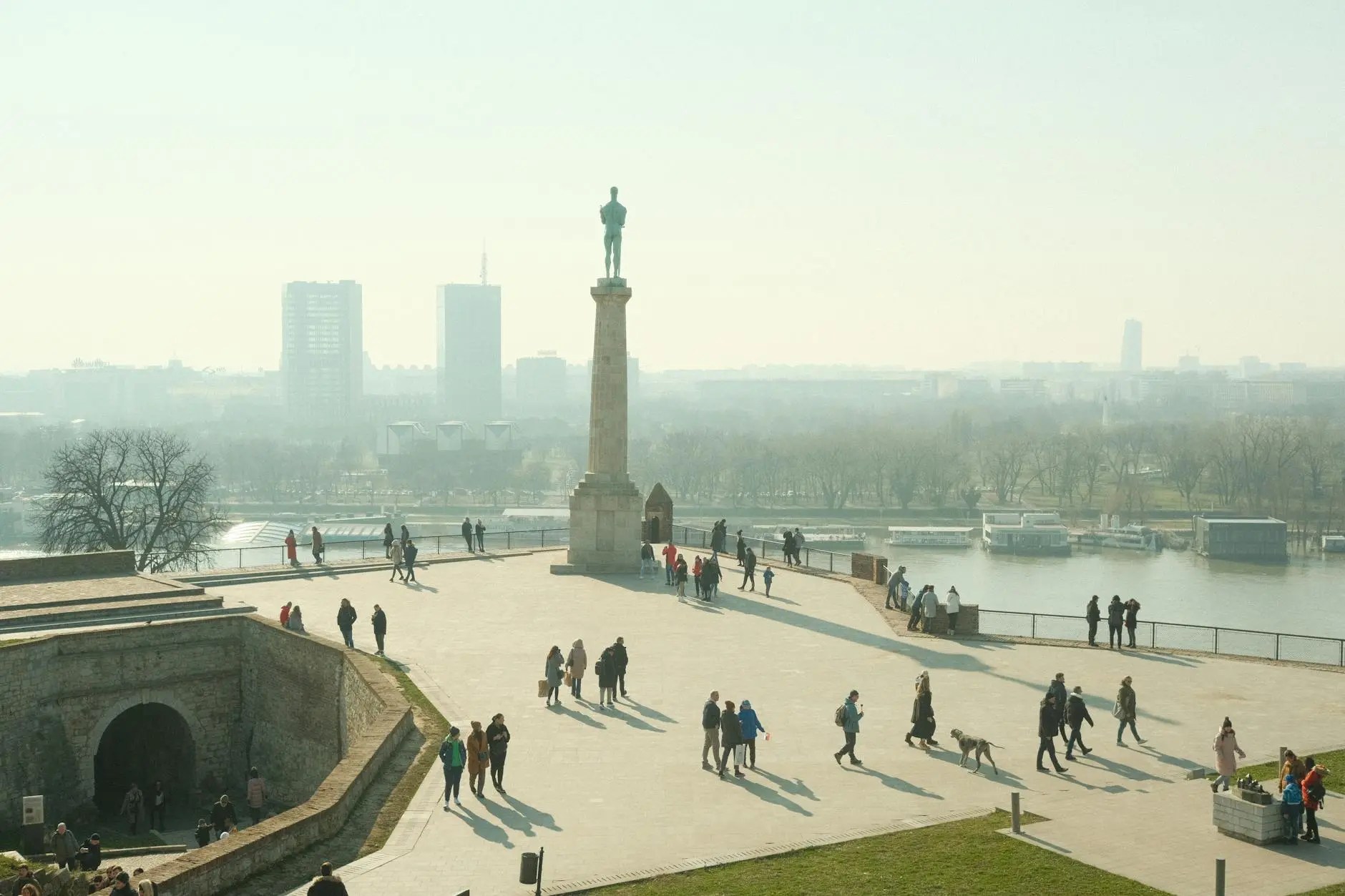 A view of Kalemegdan Fortress in Belgrade, with people walking on the grounds and the confluence of the Sava and Danube rivers in the background.