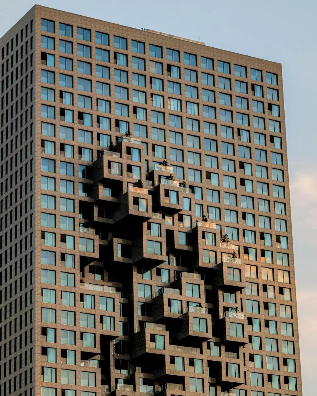 A modern building with a unique architectural design featuring protruding balconies and large glass windows, set against a sky backdrop.