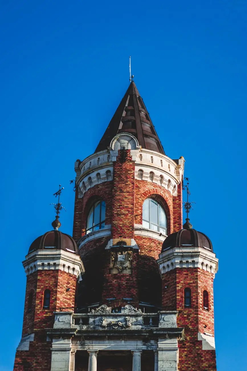 Close-up view of a tall, ornate tower with a cone-shaped roof and decorative brickwork against a clear blue sky.