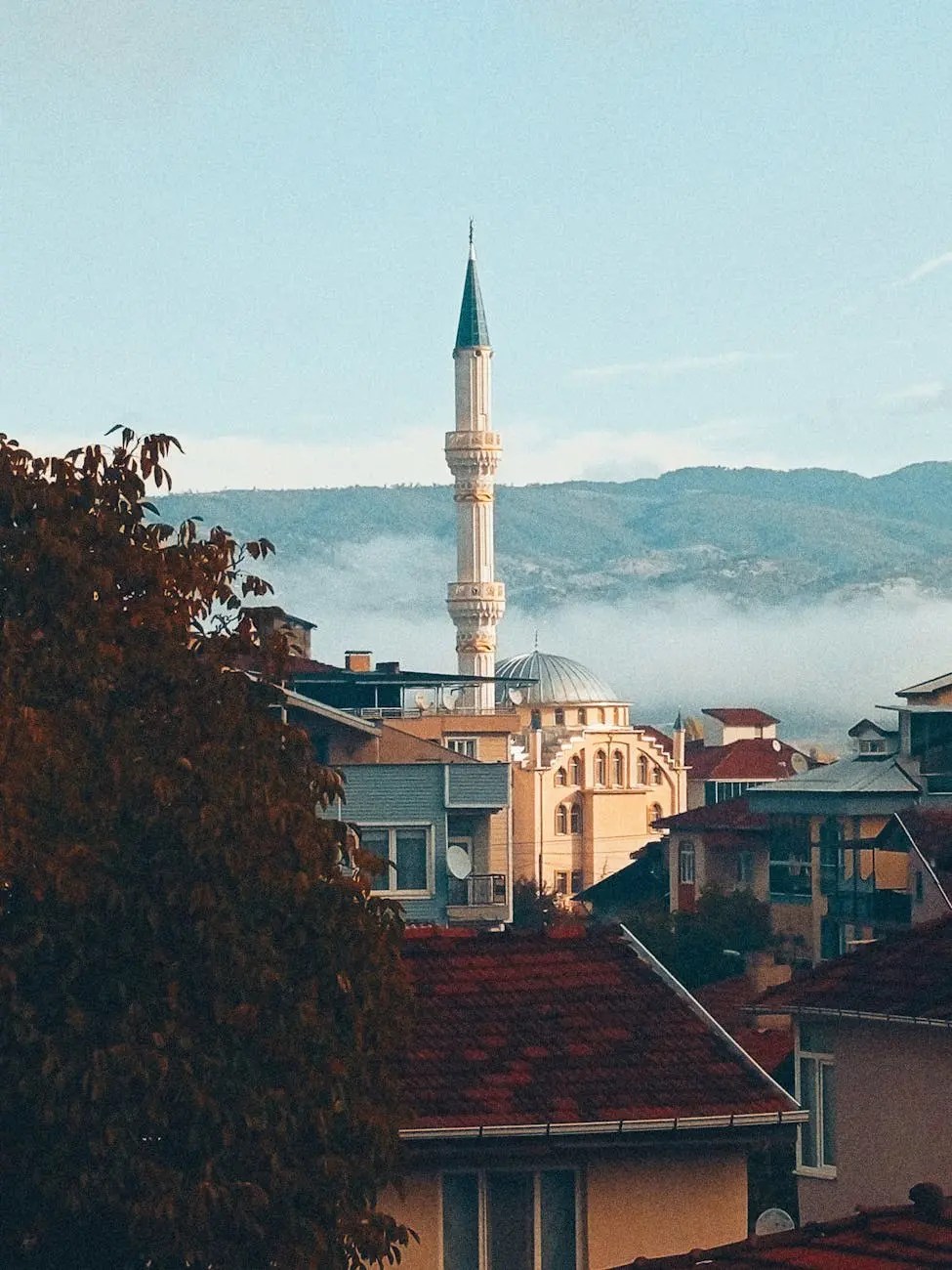 View of a mosque's minaret and surrounding buildings in Sarajevo, with mountains in the background.
