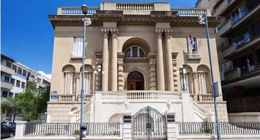 A grand historical building featuring classic architectural elements, with large columns, ornate details, and a serene entrance, located in a sunny urban setting.