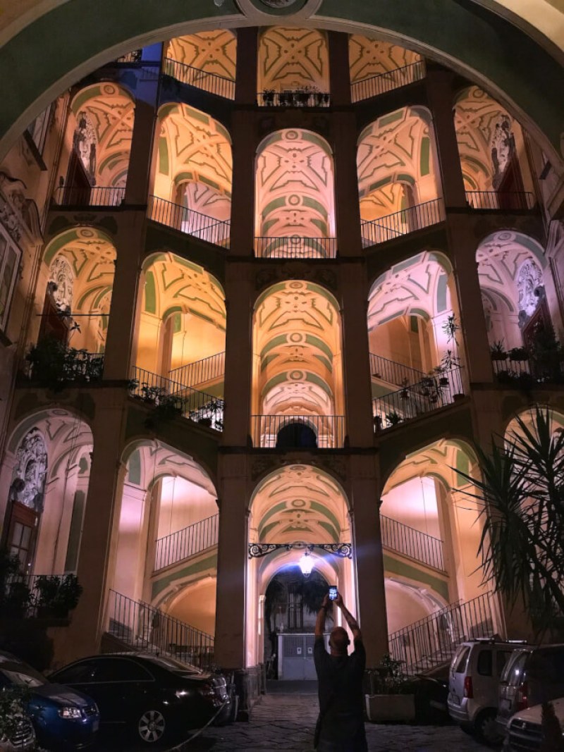 Night view of a beautifully illuminated historic atrium in Naples, showcasing intricate architectural details and vibrant colors.