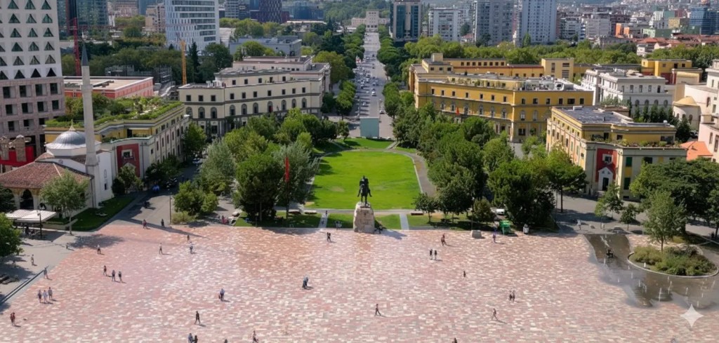 Aerial view of Skanderbeg Square in Tirana, Albania, featuring a statue in the center surrounded by green trees and colorful buildings.