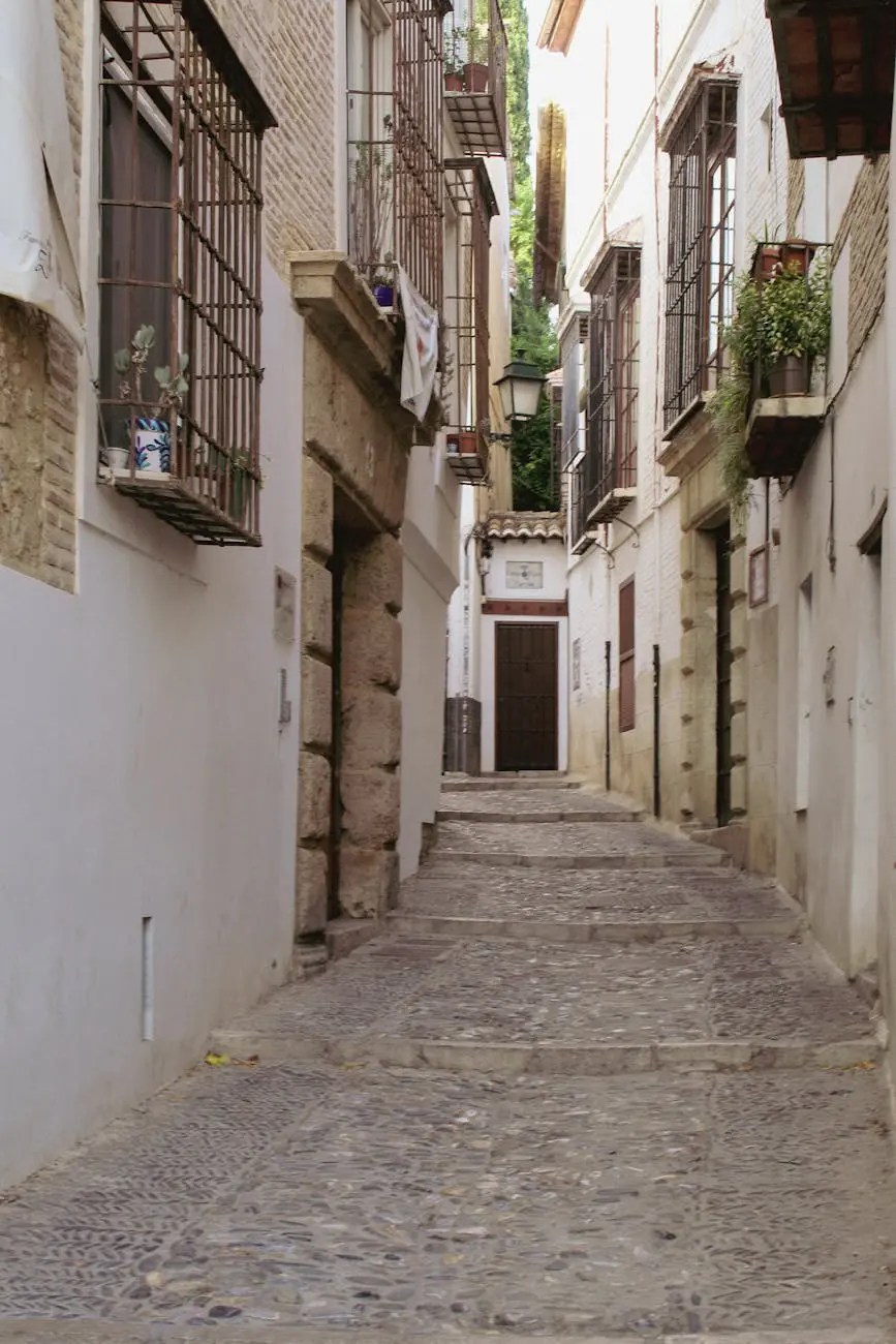 A narrow cobblestone street in Granada, Spain, lined with whitewashed buildings featuring wrought iron balconies and greenery.